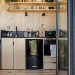 Cuisine moderne en bois dans un hébergement insolite, avec étagères et plantes décoratives.