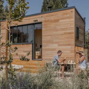 Cabane en bois moderne, entourée de verdure, avec une terrasse et des occupants profitant d'un
