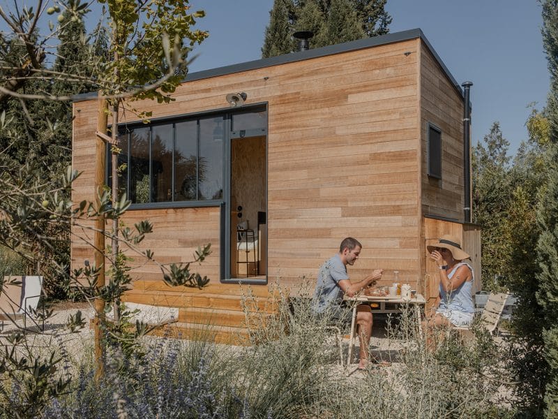 Cabane en bois moderne avec terrasse, couple profitant dun repas en plein air.