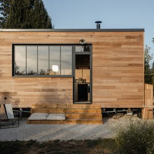 Tiny house en bois avec grandes fenêtres, terrasse en bois et coin détente extérieur.
