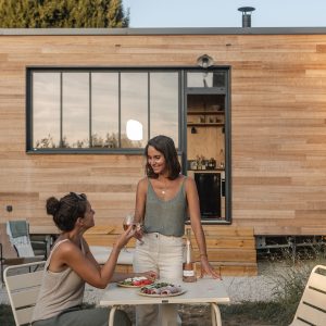 Deux amies profitent d'un repas en extérieur devant une maison en bois moderne.