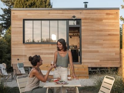 Deux amies profitent d'un repas en extérieur devant une maison en bois moderne.