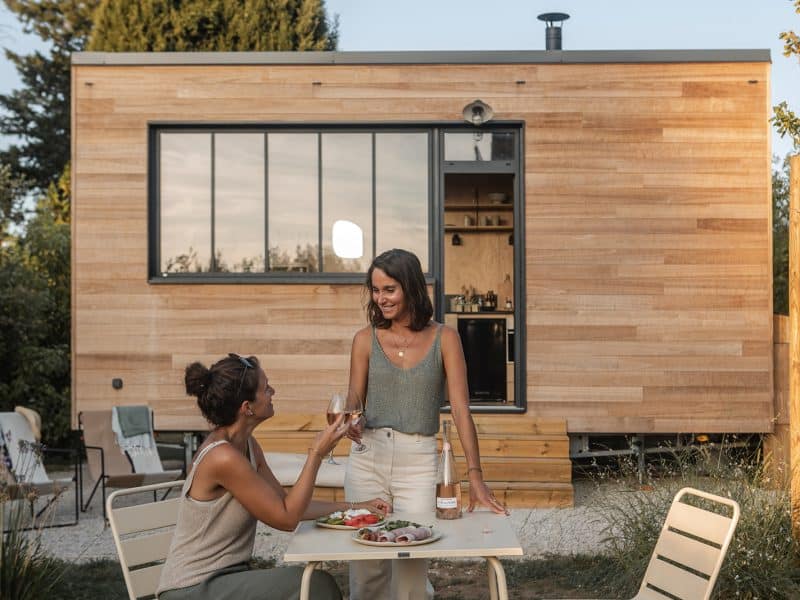 Chalet moderne en bois avec terrasse, deux femmes savourent un repas convivial.