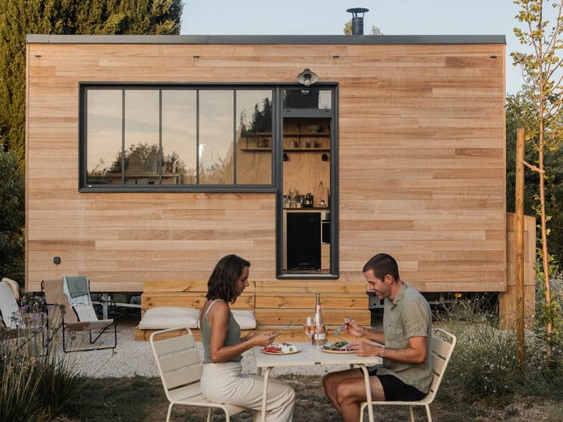 Cabane moderne en bois avec terrasse, couple dînant en plein air.