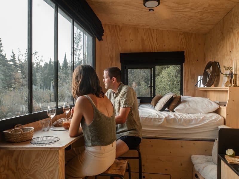 Cabane moderne avec vue panoramique, couple dégustant un repas près de la fenêtre.