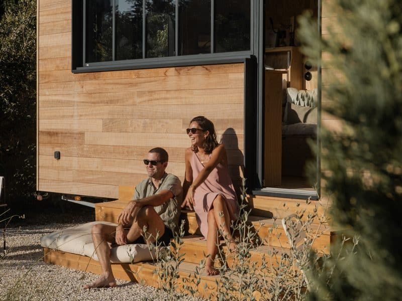 Cabane en bois avec terrasse, couple détendu profitant du soleil.