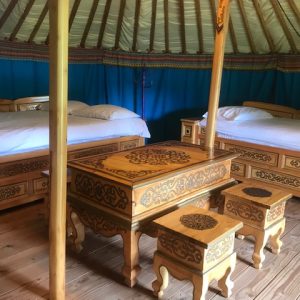 Intérieur d'une yourte traditionnelle, avec lits en bois sculpté et décor coloré.