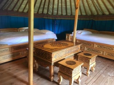 Intérieur d'une yourte traditionnelle, avec lits en bois sculpté et décor coloré.