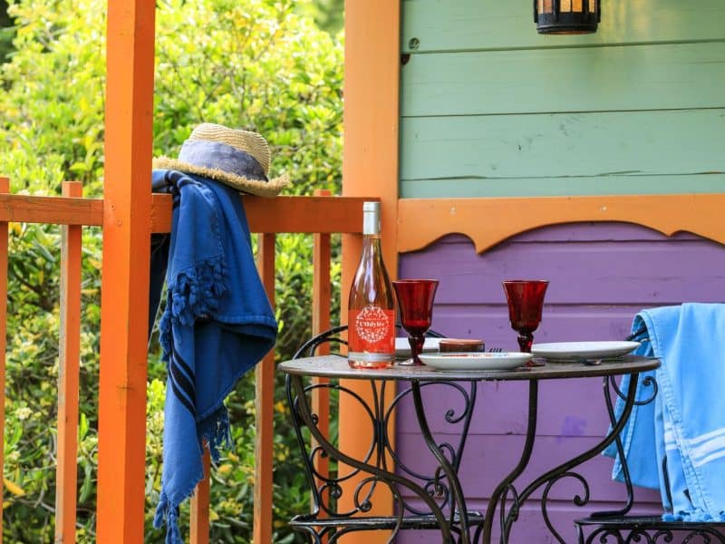 Charmante cabane colorée avec terrasse, table en fer forgé et vue sur la verdure.