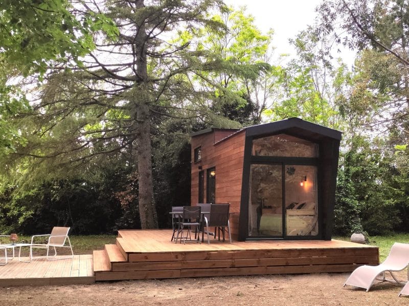 Cabane moderne en bois avec terrasse en bois et mobilier de jardin, entourée darbres.