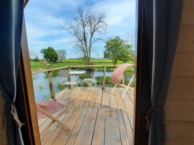 Cabane sur pilotis avec vue sur un étang et chaises confortables sur la terrasse.