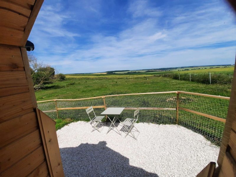 Cabane en bois avec terrasse, vue dégagée sur la campagne verdoyante.