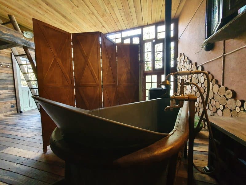 Cabane en bois avec baignoire vintage et parois en bois, ambiance chaleureuse.