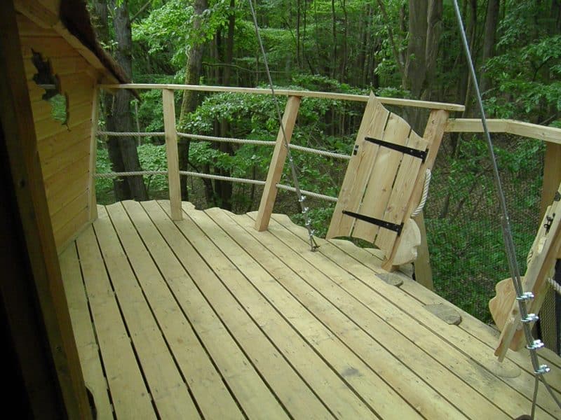 Cabane dans les arbres avec terrasse en bois, entourée de verdure luxuriante.