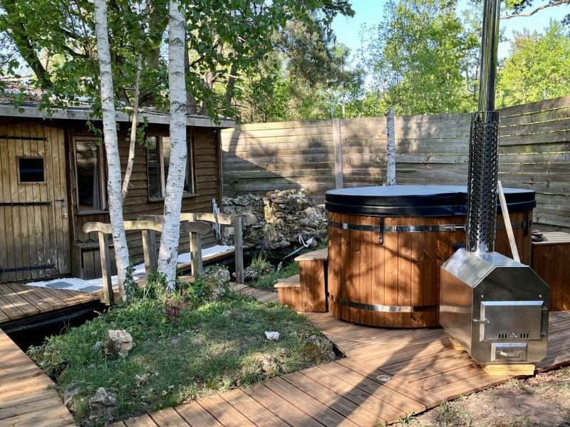 Hébergement insolite en bois avec un bain nordique, entouré de verdure apaisante.