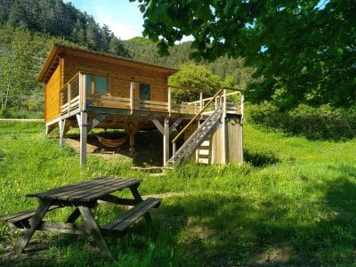 Cabane en bois sur pilotis, entourée de verdure, avec une table de pique-nique.