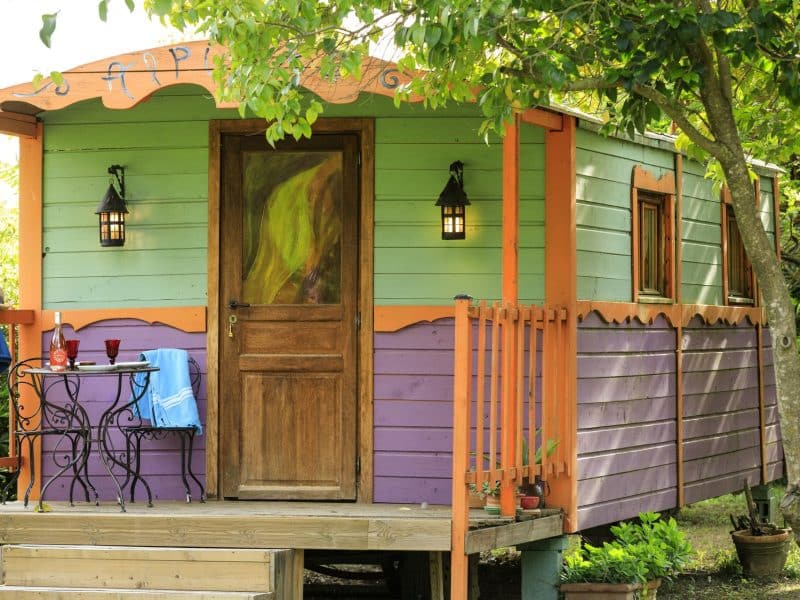 Charmante cabane colorée avec terrasse, entourée de verdure. Parfaite pour un séjour relaxant.