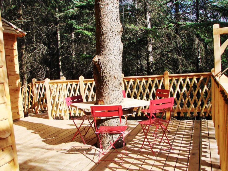 Cabane en bois avec terrasse en bois et table ronde entourée de chaises rouges.