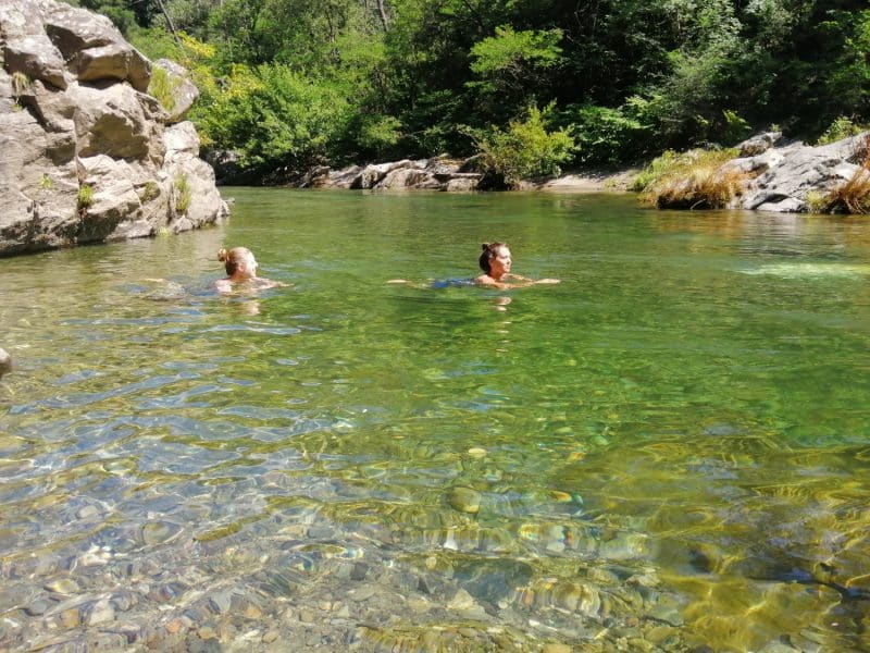 Deux baigneurs profitent dune piscine naturelle entourée de rochers et de verdure.