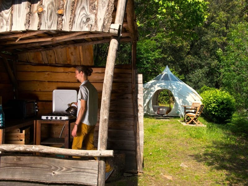 Cabane en bois avec kitchenette, à côté dune tente géodésique dans la nature.