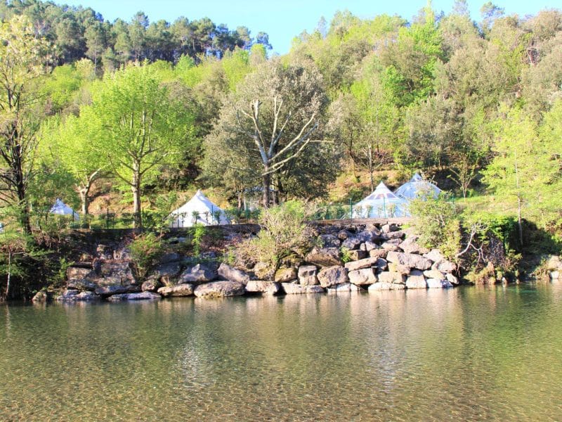 Tentes de glamping au bord dune rivière, entourées de verdure luxuriante.