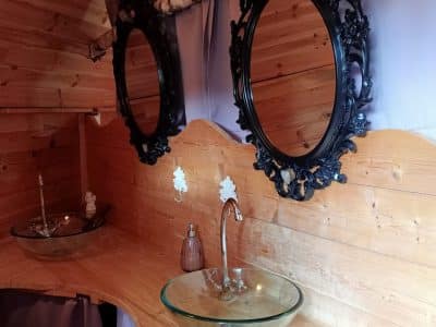 Salle de bain dun hébergement insolite en bois, avec miroirs élégants et vasques en verre.