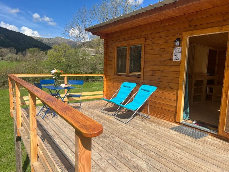 Chalet en bois avec terrasse, chaises longues et vue sur la nature environnante.