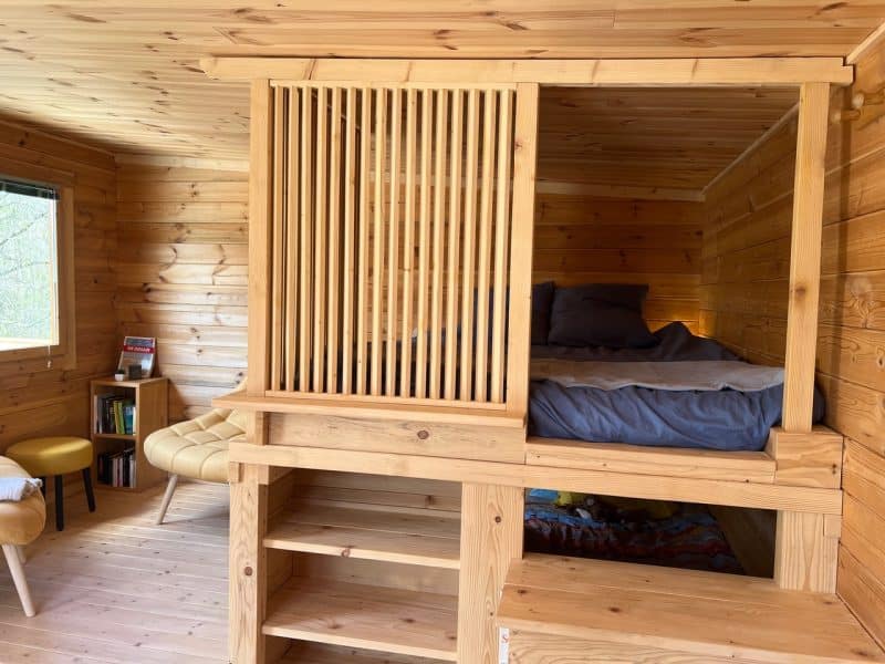 Cabane en bois avec un lit surélevé et un intérieur chaleureux en bois naturel.