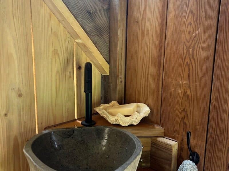 Cabane en bois avec lavabo en pierre et décor naturel chaleureux.