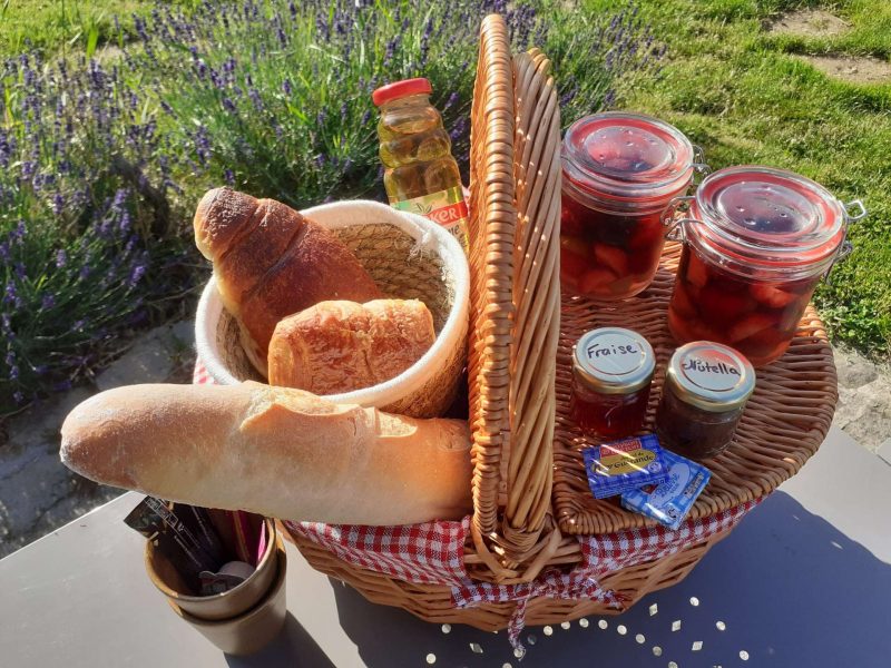 Panier pique-nique en osier avec pains, confitures et boissons, idéal pour un séjour champêtre.