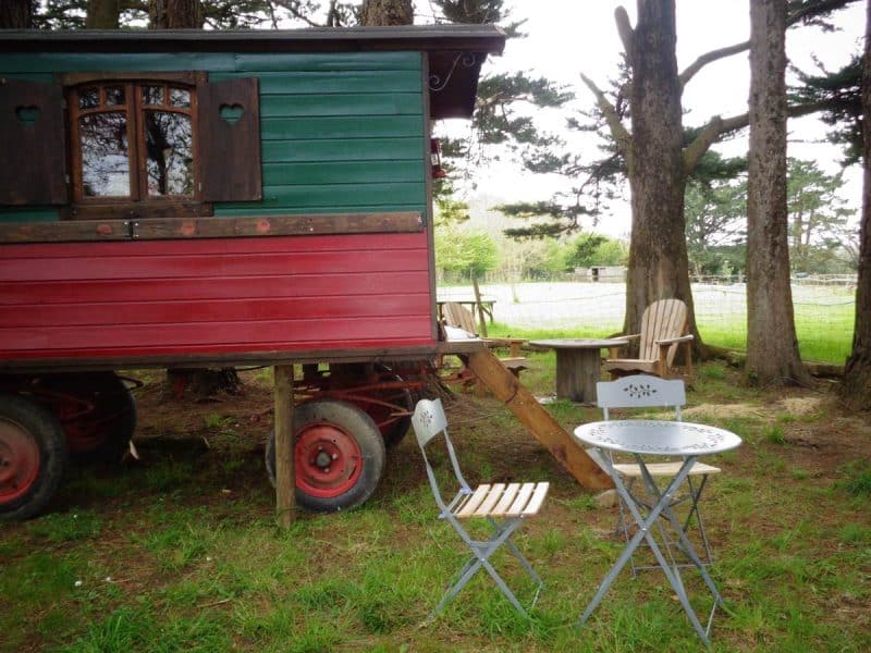Charmante roulotte colorée en Bretagne, entourée darbres et dun coin repas.