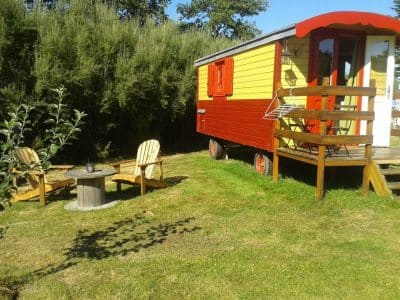 Roulotte colorée en Bretagne, avec chaises en bois et espace verdoyant.