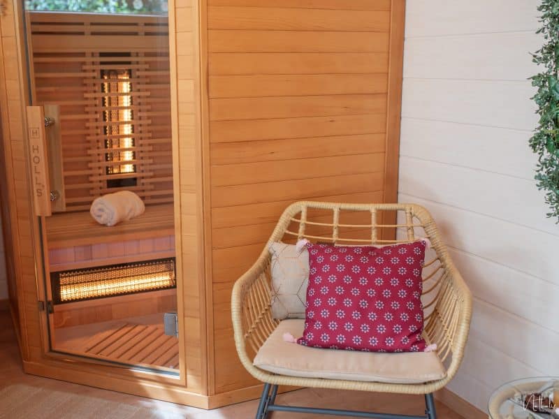 Sauna en bois avec fauteuil en rotin et coussin décoratif rouge, ambiance relaxante.
