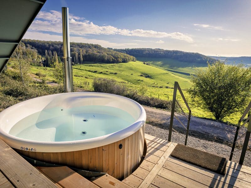 Hébergement en chalet avec jacuzzi, vue panoramique sur la campagne verdoyante.