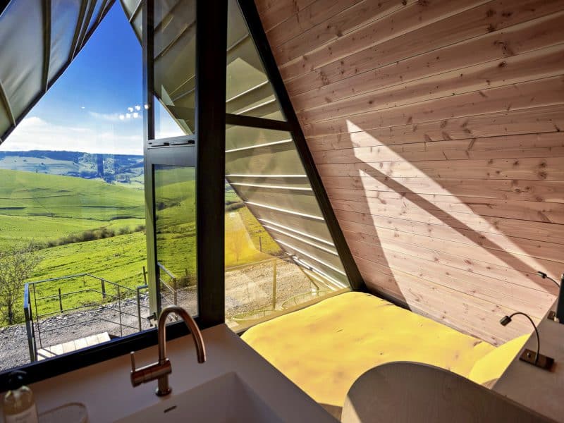 Cabane moderne avec vue panoramique sur la verdure et lumière naturelle abondante.