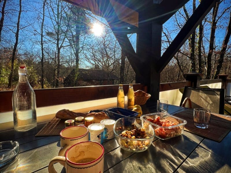 Chalet en bois avec petit-déjeuner en terrasse, soleil levant et nature environnante.