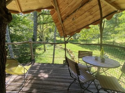 Cabane perchée en Midi-Pyrénées avec terrasse en bois et vue sur la nature verdoyante.