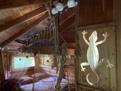 Cabane en bois avec lit suspendu et décorations lumineuses, ambiance chaleureuse.