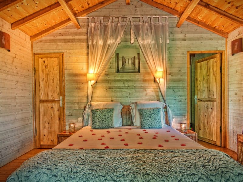 Chalet romantique avec lit douillet, décoré de pétales de rose et lumière douce.