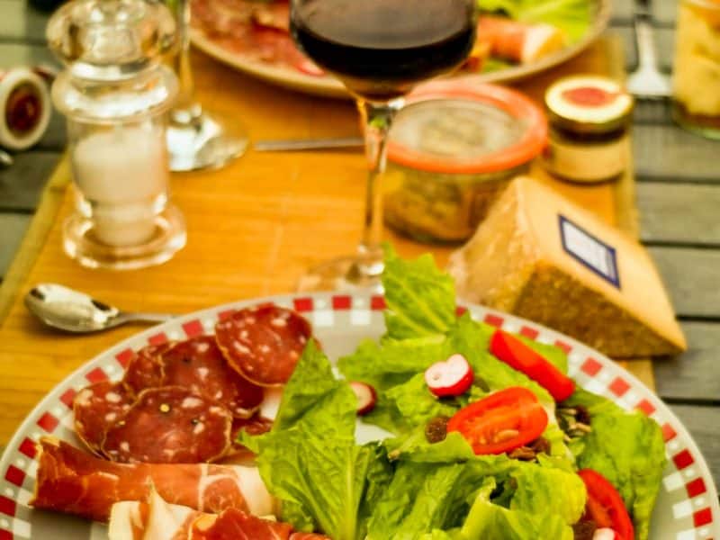 Dégustation de charcuterie et vin rouge sur une table en extérieur, ambiance conviviale.