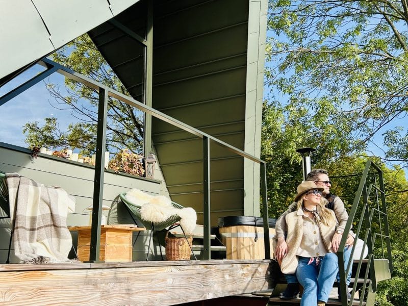 Cabane moderne en bois avec un toit en pente, couple détendu sur les marches.