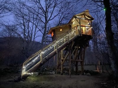 Cabane perchée illuminée, nichée dans les arbres de Midi-Pyrénées, ambiance magique.