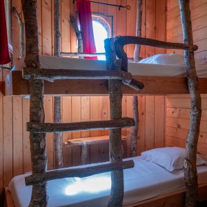 Cabane en bois avec lits superposés et échelle en branches naturelles.