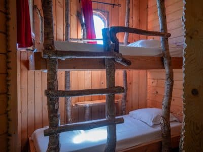 Cabane en bois avec lits superposés et échelle en branches naturelles.