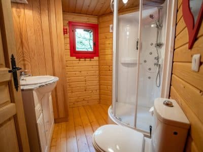 Cabane en bois avec salle de bain moderne et fenêtre rouge. Confort au cœur de la nature.