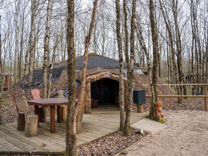 Hébergement insolite en forme de hutte, entouré darbres, avec une terrasse en bois.