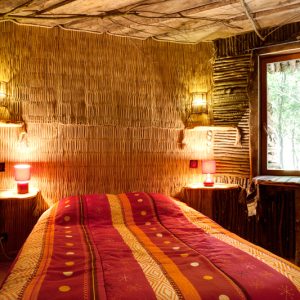 Chambre en cabane en bois, décor chaleureux avec murs en bambou et éclairage doux.