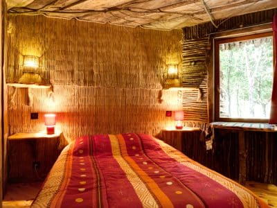 Chambre en cabane en bois, décor chaleureux avec murs en bambou et éclairage doux.