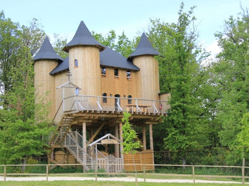 Cabane dans les arbres en forme de château, entourée de verdure luxuriante.