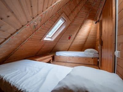 Chambre en bois sous les combles, deux lits simples et lumière naturelle.